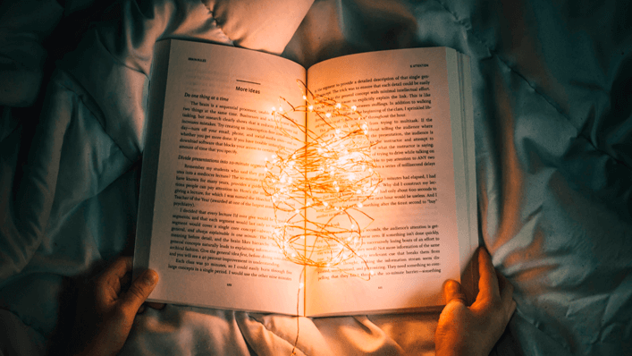 Pessoa lendo um livro na cama com luzes no meio - saúde mental