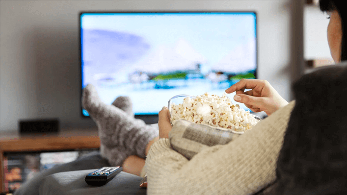 Pessoa sentada no sofá, comendo pipoca e assistindo televisão - saúde mental