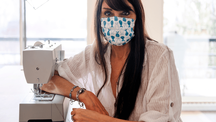 Mulher ao lado de máquina de costura para máscara caseira - coronavírus